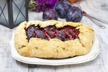 Plum galette on wooden table. Raw plums and pumpkins in the back