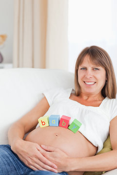 Lovely pregnant woman playing with wooden blocks while lying on