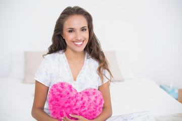 Obraz na płótnie Canvas Smiling attractive woman holding heart pillow