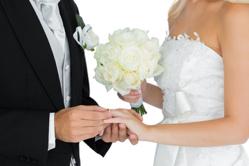 Young bridegroom putting on the wedding ring on his wife's finge