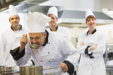 Head chef tasting a soup and smiling at camera