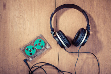 Retro compact cassette with rolls and headphones on wood