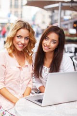 Two beautiful girls with laptop in summer cafe
