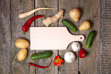 Deska do krojenia na drewnianym tle z warzywami. - obrazy, fototapety, plakaty