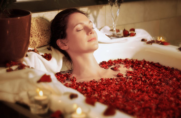 Woman relaxing in bathtub with rose blossoms