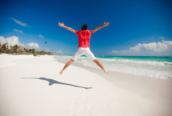 Young man jumping and raising his arms up on the beach