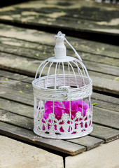 Fototapeta na wymiar Birdcage with pink flowers inside on rustic wooden table in the