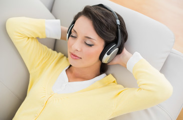 Relaxed casual brunette in yellow cardigan listening to music wi