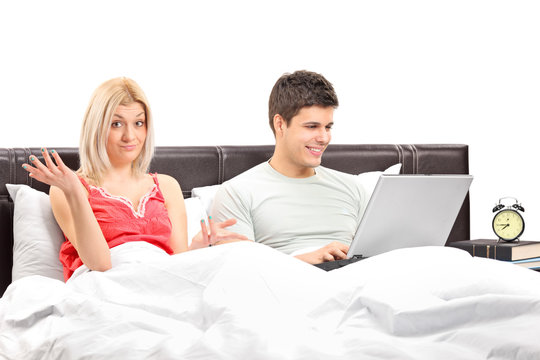 Disappointed girl in bed with her boyfriend working on a laptop