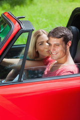 Happy blonde kissing her boyfriend in red cabriolet