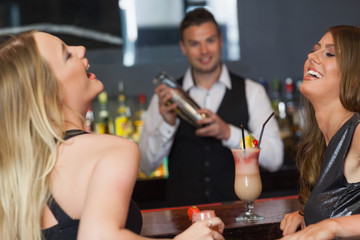 Handsome bartender working while gorgeous friends laughing