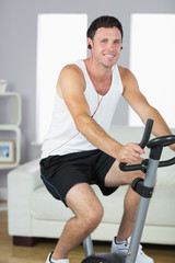 Fototapeta na wymiar Cheerful sporty man exercising on bike and listening to music