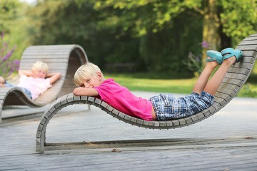 Two boys chilling out at wooden ergonomic chairs in park - obrazy, fototapety, plakaty