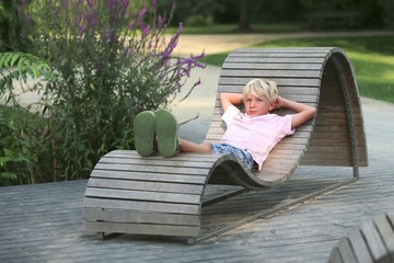 Teenager boy relaxing on a wooden bench in beautiful park