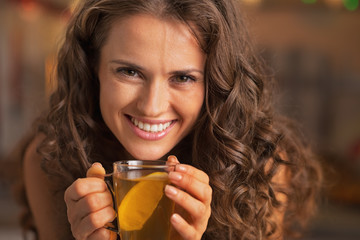 Smiling young woman drinking ginger tea with lemon