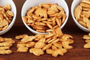Delicious crackers in bowls on wooden table on brown background