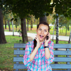 A portrait of a smiling woman in a park on a bench talking on th