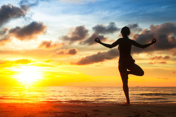 Fototapeta na wymiar Silhouette of young woman practicing yoga on the beach