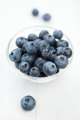 Glass bowl with blueberries on white wooden board, vertical shot