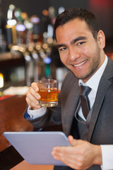 Cheerful businessman working on his tablet while having a whiske