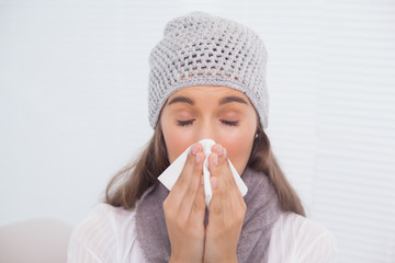 Cute brunette with winter hat on blowing her nose