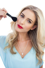 Thoughtful blonde model in blue dress applying make up