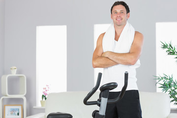 Cheerful sporty man standing next to exercise bike cross armed