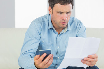 Serious casual man holding calculator paying bills looking at do