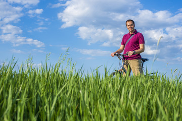Young man standing with bicycle on a green grass