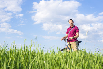 Young man standing with bicycle on a green grass