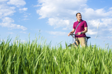 Young man standing with bicycle on a green grass