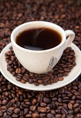 A cup of black coffee  with coffee beans around