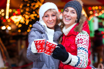 Freunde trinken Glühwein auf Weihnachtsmarkt zur Adventszeit