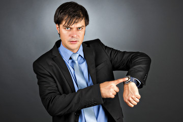 Young businessman pointing to his watch with an angry expression
