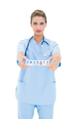 Serious brown haired nurse in blue scrubs showing a medication b