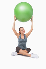 Sporty young woman lifting a green fitness ball
