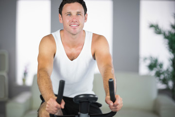 Naklejka na ściany i meble Attractive fit man exercising on bike smiling at camera