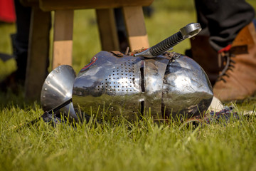 Helmet of the medieval knight and the sword on the green field.