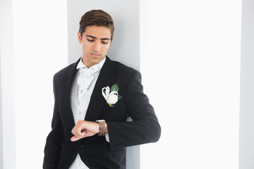 Serious bridegroom leaning against wall