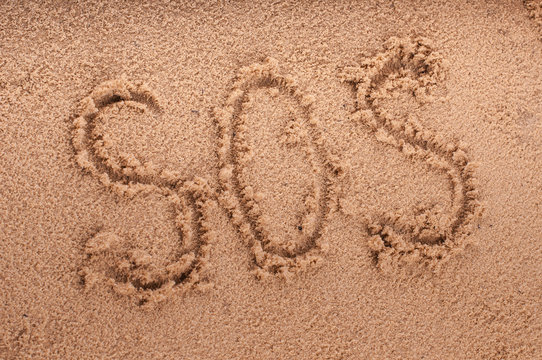SOS on the beach sand at the sea.