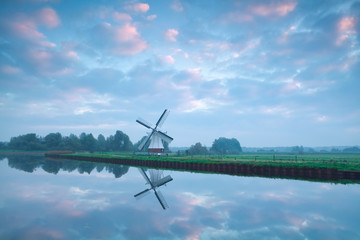 Fototapeta na wymiar charming Dutch windmill by river during sunrise