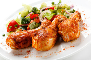 Grilled chicken legs and vegetables on white background