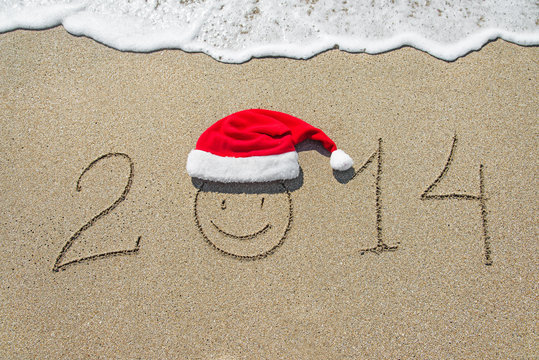 happy new year 2014 with smiley face in christmas hat on sandy b