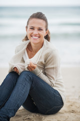 Fototapeta na wymiar Happy woman wrapping in sweater while sitting on lonely beach