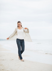 Smiling young woman in sweater walking on lonely beach