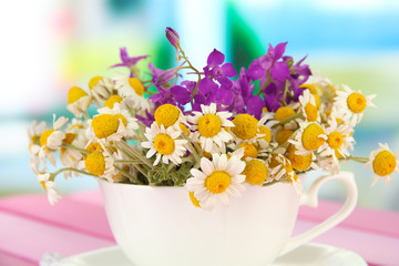 Bouquet of chamomile flowers in cup, on bright background