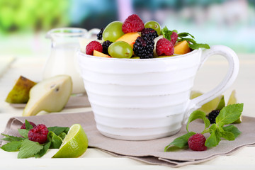 Fruit salad in cup on wooden table on nature background