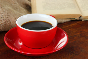 Cup of coffee and book on wooden table on sackcloth background