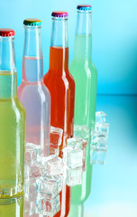 Drinks in glass bottles with ice cubes on blue background