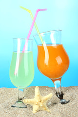 Beach cocktails in sand on blue background